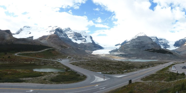 Foto des Athabasca Gletschers. Im Vordergrund sind der Parkway Highway, sowie Parkplätze sowie Seen zu sehen.
