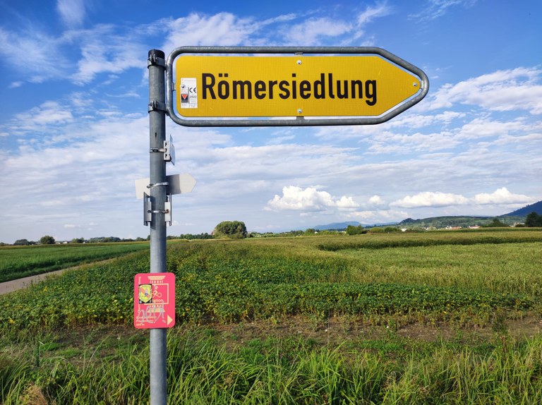 Gelbes Straßenschild der Römersiedlung Friesenheim mit der Aufschrift Römersiedlung.